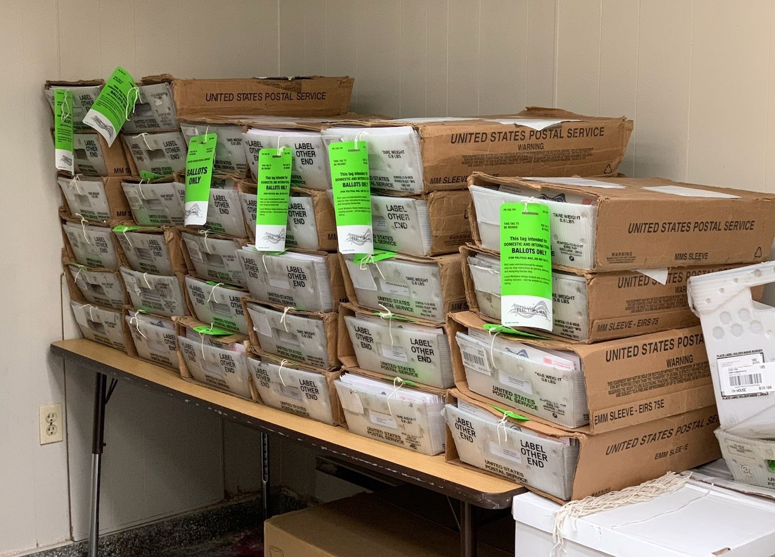 Several stacks of US Postal Service trays packed with mail-in ballots requested by voters.